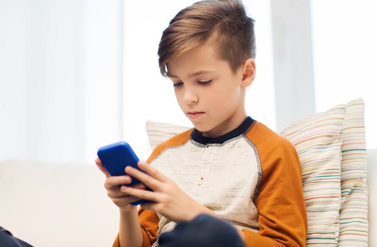 A young boy looks at his phone while sitting at home.