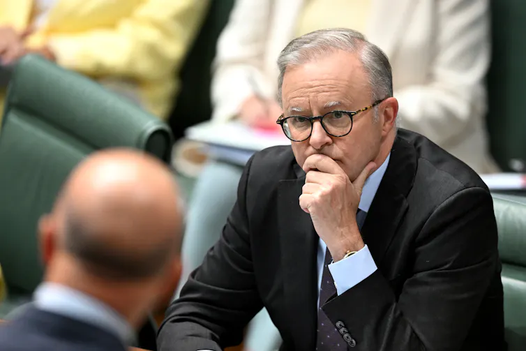 A man in a suit and glasses looks thoughtful