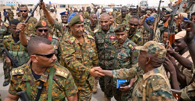 An army general shakes hands with uniformed troops.