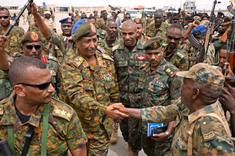 An army general shakes hands with uniformed troops.