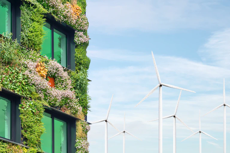 Left side, building with windows, walls covered in green plants, right side blue sky and a dozen white wind turbines