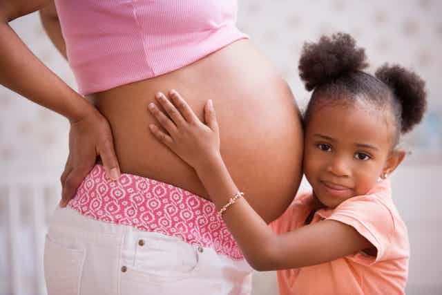 Young child touches a woman's pregnant belly