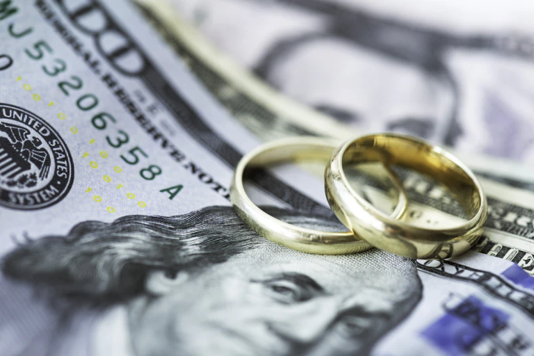 Two gold wedding rings atop US bills
