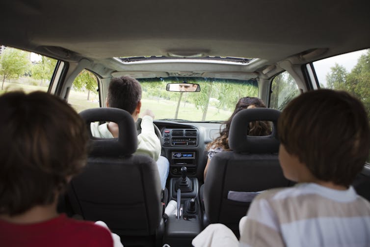 A camera in the back of a minivan captures two adults riding in the front seat and two brunette children sitting in the back row.