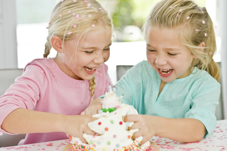 Two grinning children dig their hands into a cake.
