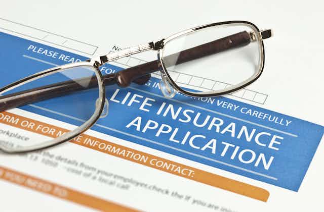 a pair of reading glasses rests on a life insurance application