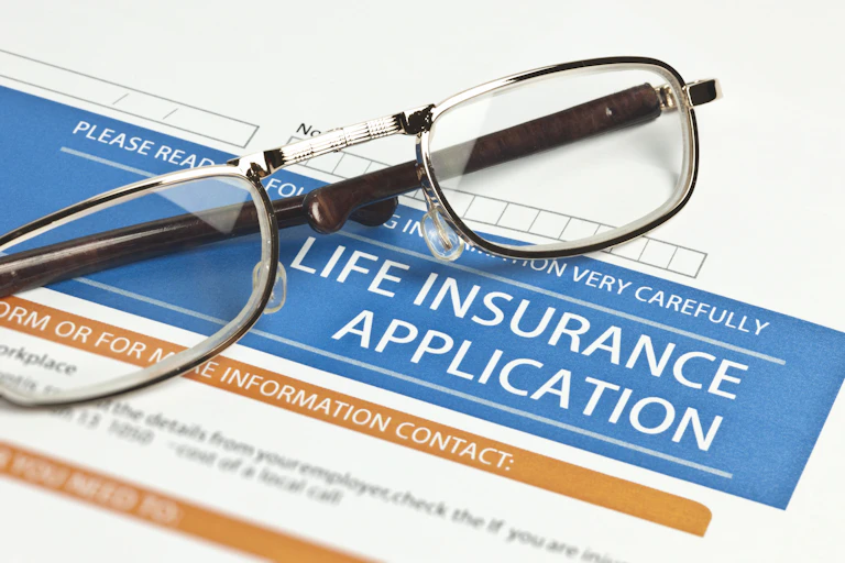 a pair of reading glasses rests on a life insurance application