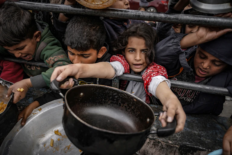 A girl holds out an empty pan while boys surround her.