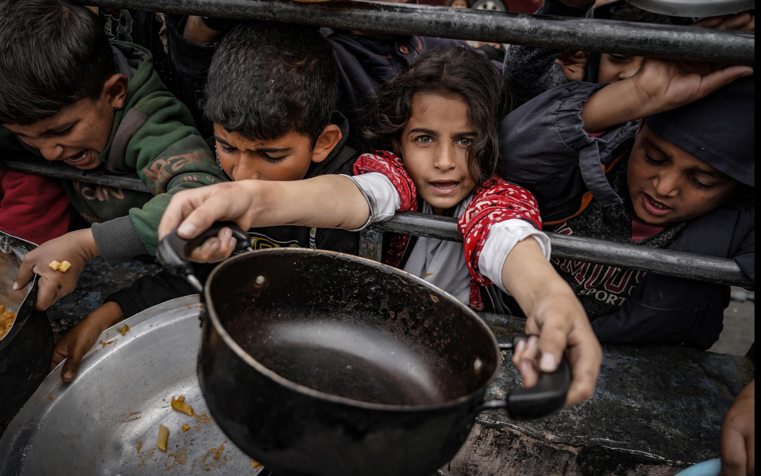 A girl holds out an empty pan while boys surround her.
