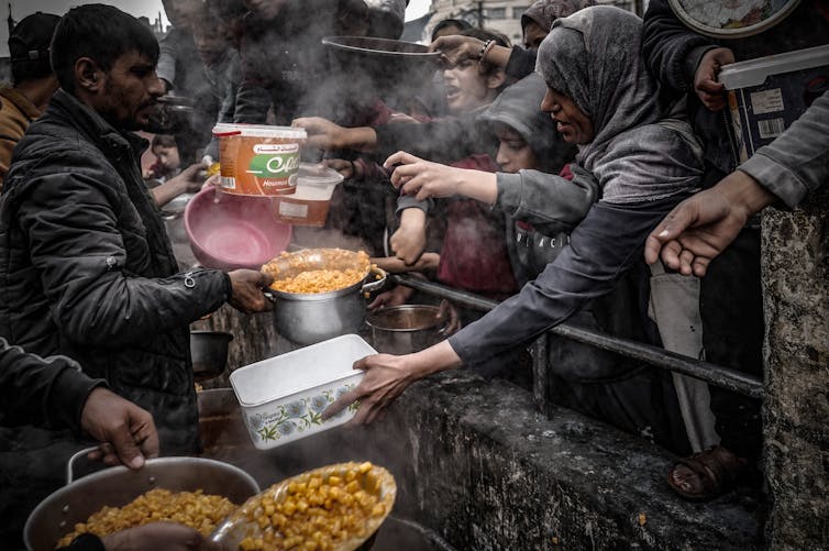 A man delivers food to a throng of people behind a fence.