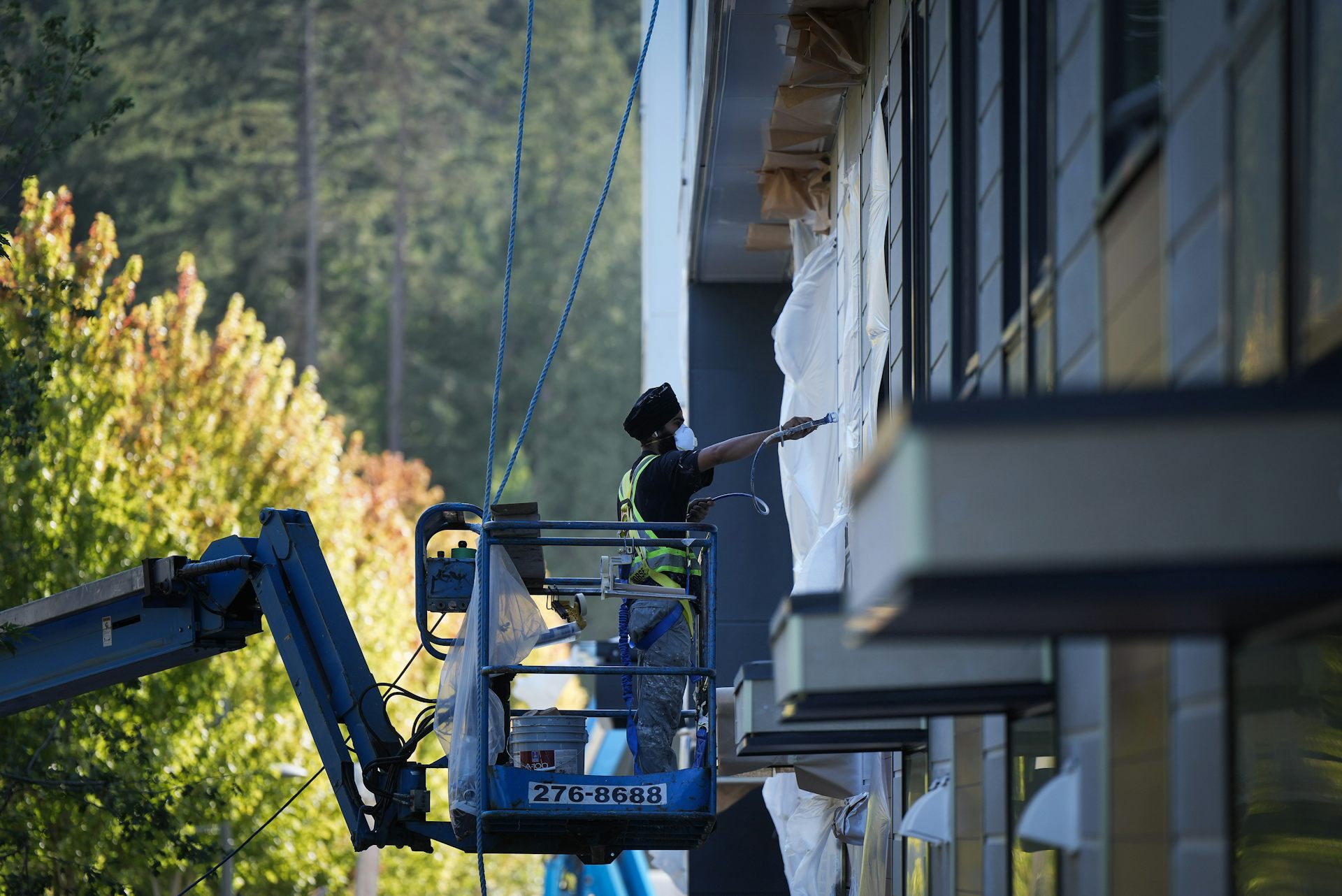 A man standing on a lift paints the outside of a building.