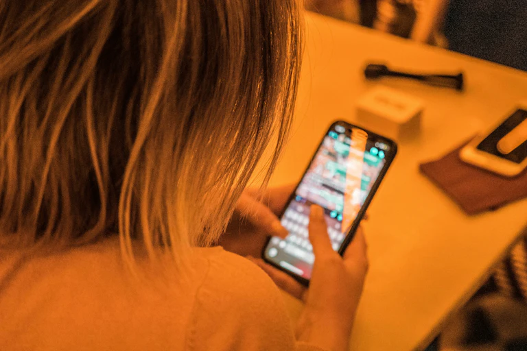 A blonde woman sitting at a table messaging on her phone