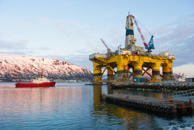 A yellow oil platform in a fjord with a red ship nearby.