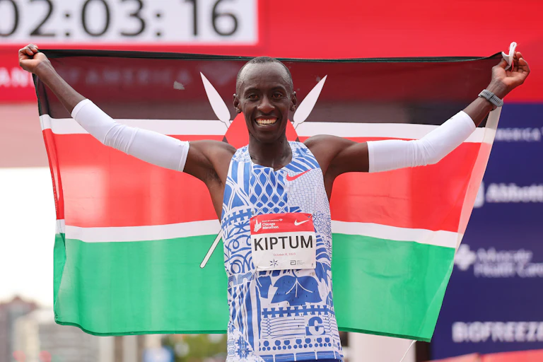 A smiling man in a running vest raises his arms, holding a black, red and green flag.