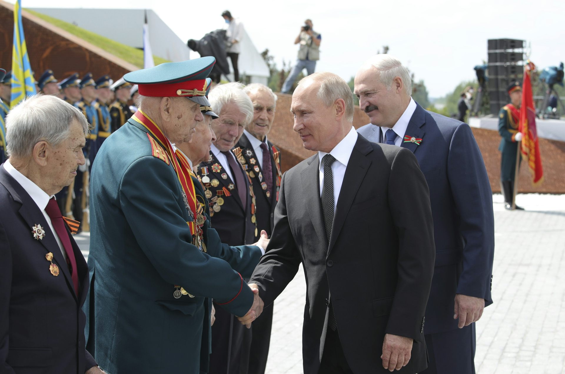 Two bald men are shaking hands with an elderly man in military uniform.