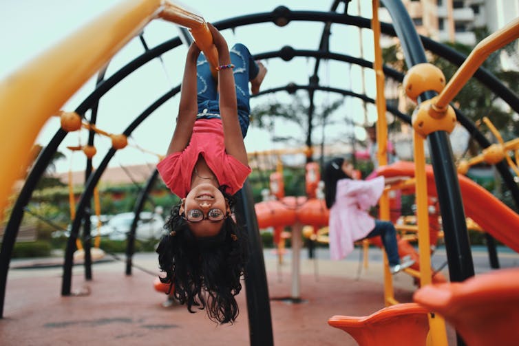 Child hangs upside down on playground equipment