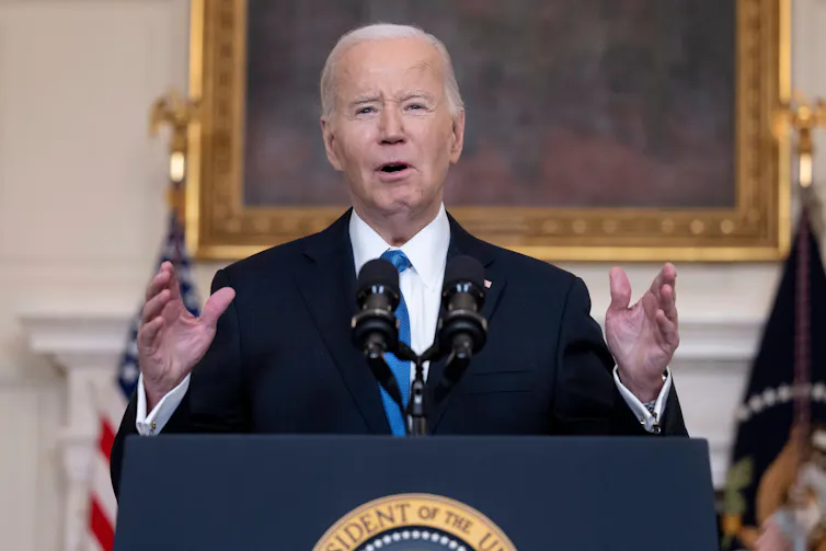 US president Joe Biden stands at a lectern in the White House gesturing with both hands.