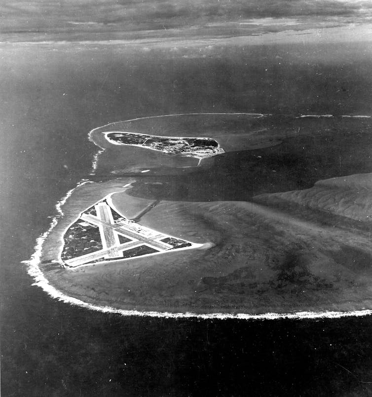 A black and white aerial photo of two small island. The one in the foreground has three intersecting landing strips.