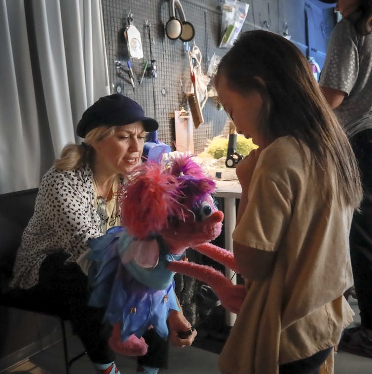 Puppeteer holding muppet Abby Cadabby out for a child to engage with