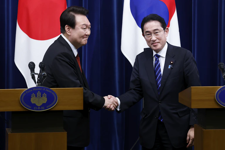 Two men shake hands in front of flags.