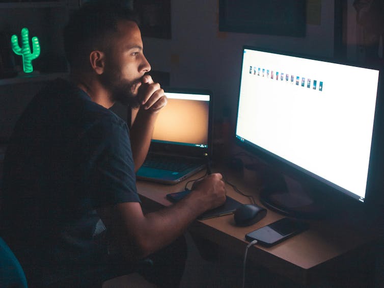 A man sitting at his home computer at night looking at files