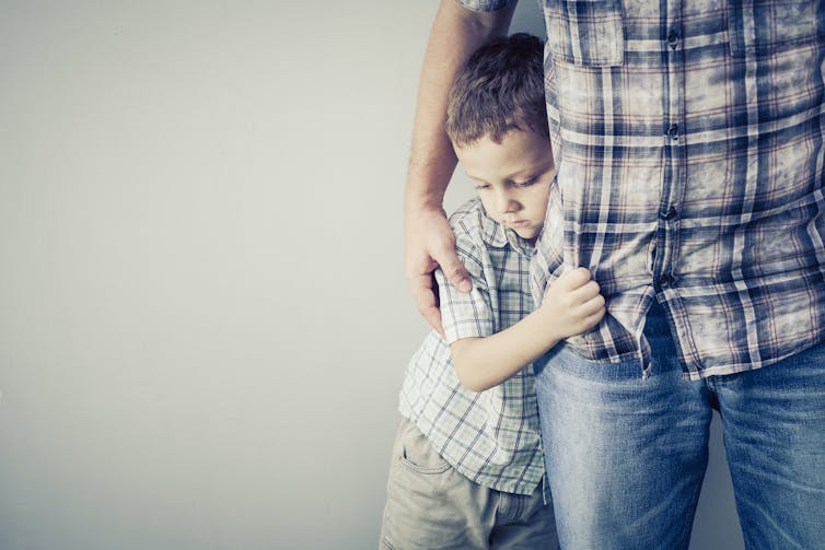 A young boy hugs the leg of his dad