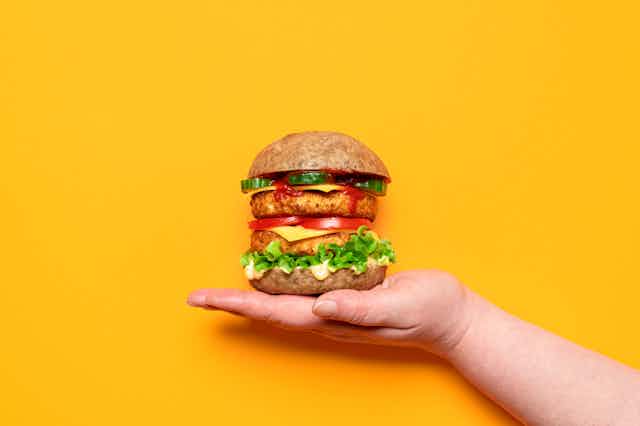 Veggie burger on upturned palm against yellow background