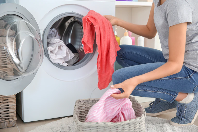 A young woman loading clothes into a washing machine at home