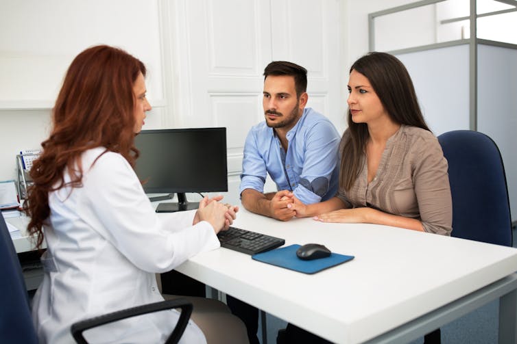 a couple sit across from a doctor in a white coat