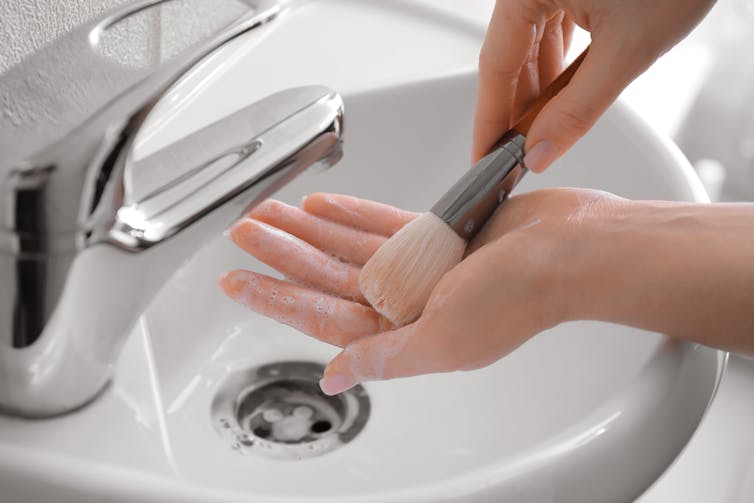 A woman washes a makeup brush in a sink.
