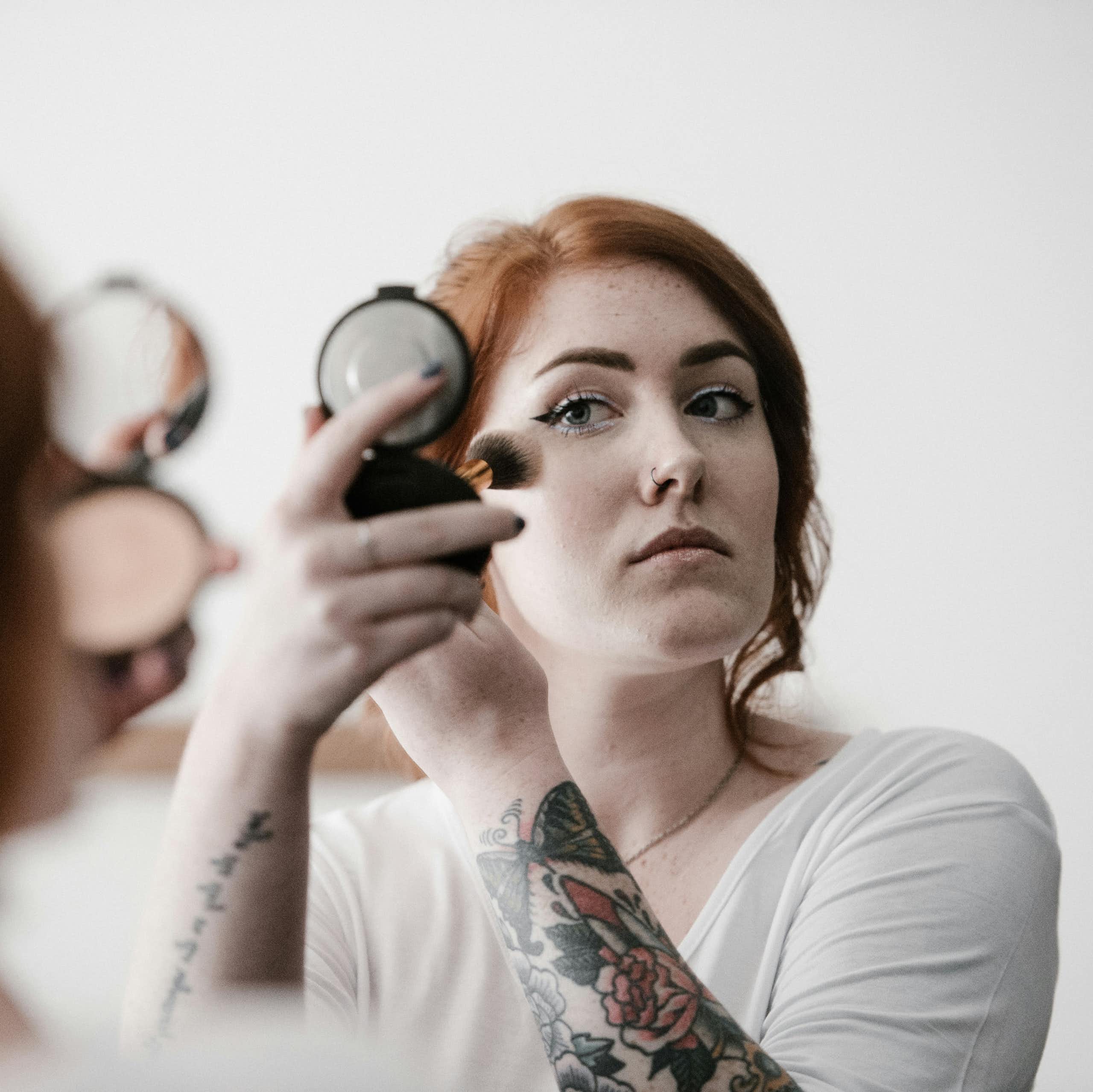 A redhaired woman applies makeup while looking in a compact mirror.