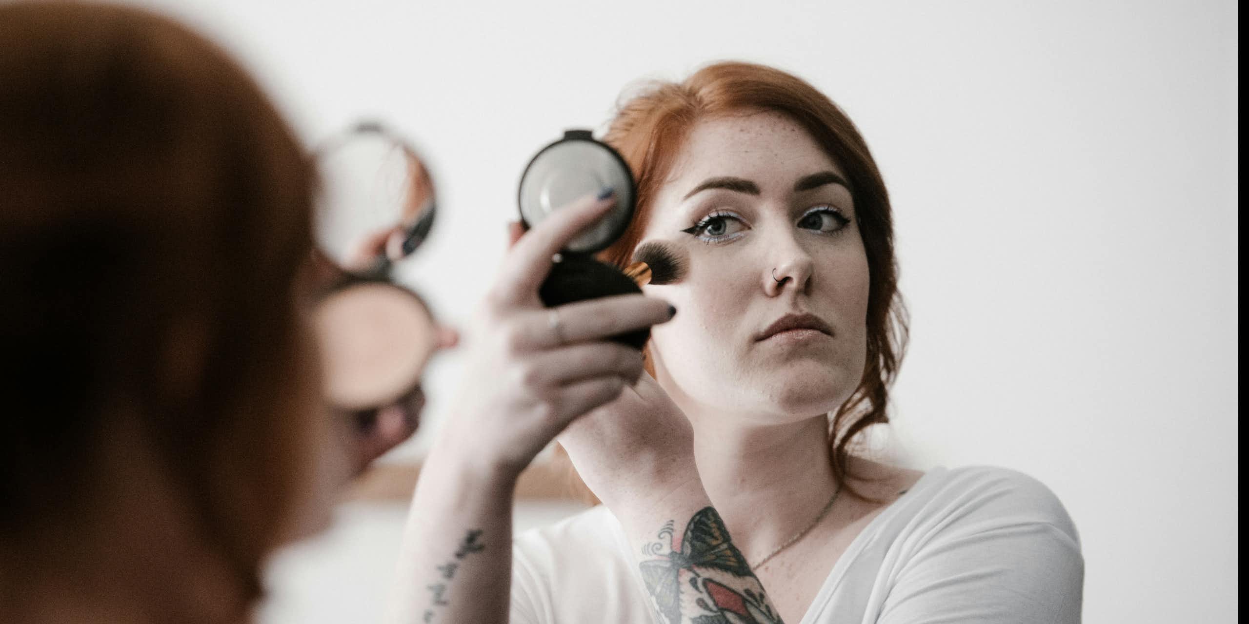 A redhaired woman applies makeup while looking in a compact mirror.