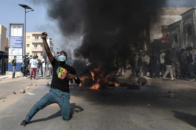 Un homme à genoux lève le point derriere une barricade en feu.