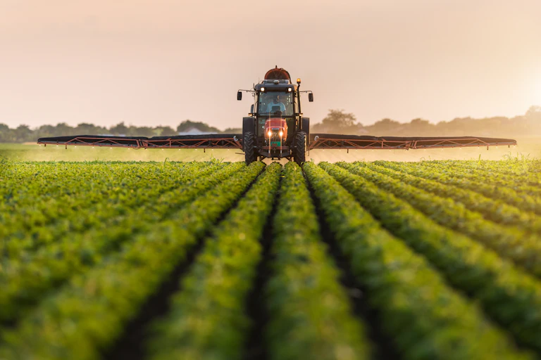 Photo d’un tracteur en train d’épandre des produits sur des cultures, vu de face.