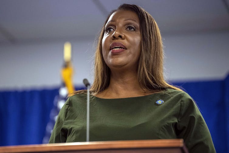 Woman with long hair stands at a podium, looking off into the audience.