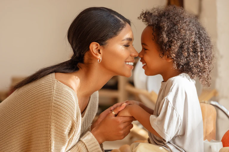 A woman seen holding a child's hands and touching noses.