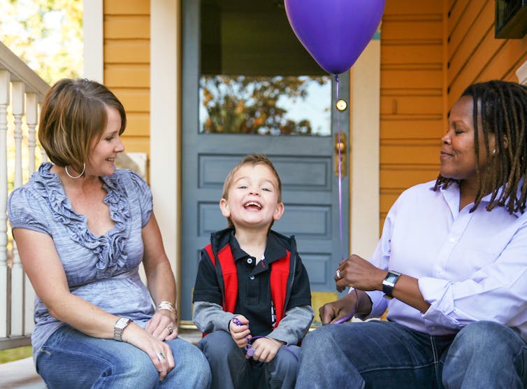 Two adults sitting on a porch with a child.