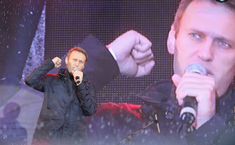 Russian politician Alexei Navalny gestures to the crowd while giving a speech -- his image appears on a big screen behind him.