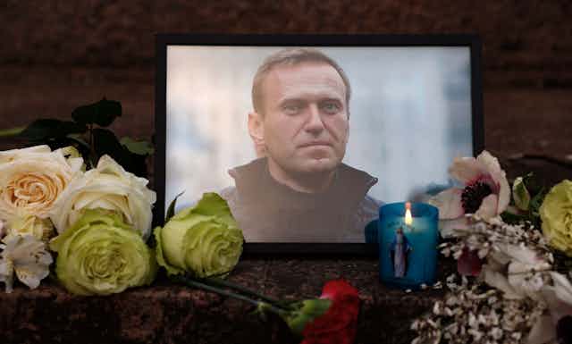 Flowers and candles are left next to a photo of a man in a coat.