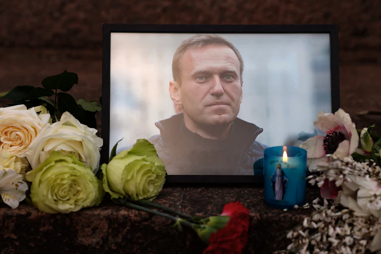 Flowers and candles are left next to a photo of a man in a coat.