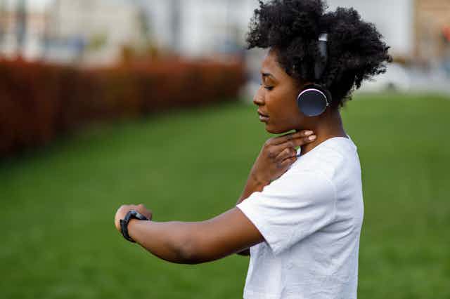 Athlete wearing headphones with fingers pressed to pulse on neck, looking at watch