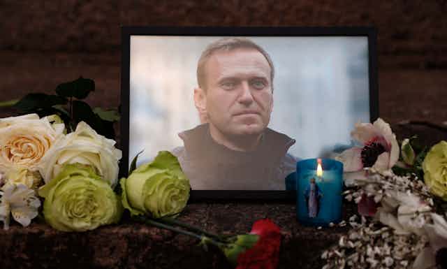 Flores e velas são deixadas ao lado de uma foto de um homem de paletó.