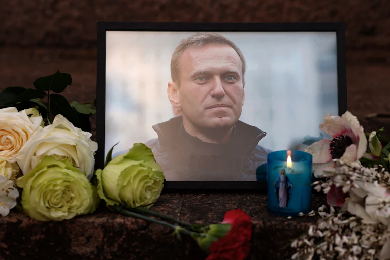 Flores e velas são deixadas ao lado de uma foto de um homem de paletó.