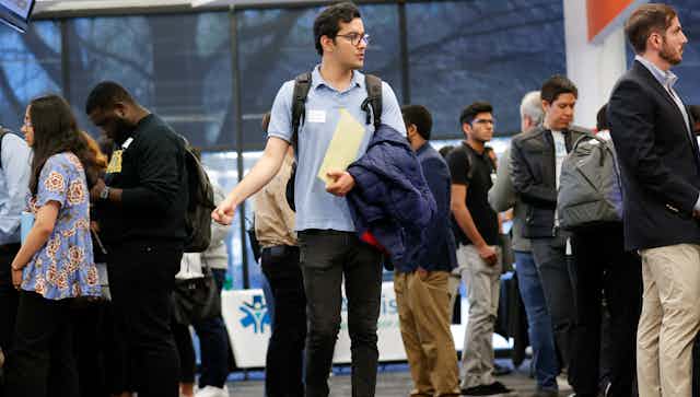A person seen clutching a dossier wearing a name tag browsing a job fair.