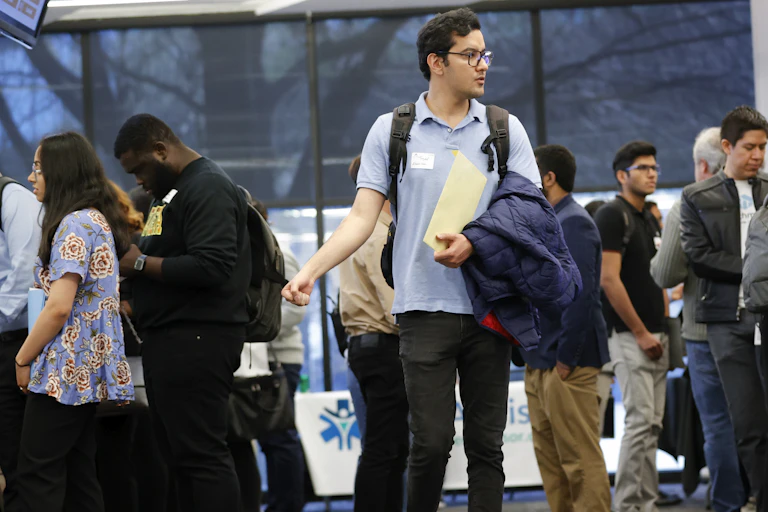 A person seen clutching a dossier wearing a name tag browsing a job fair.