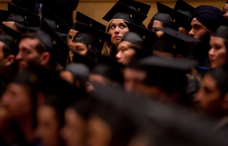 A student seen in cap and gown looking up at a graduation ceremony.