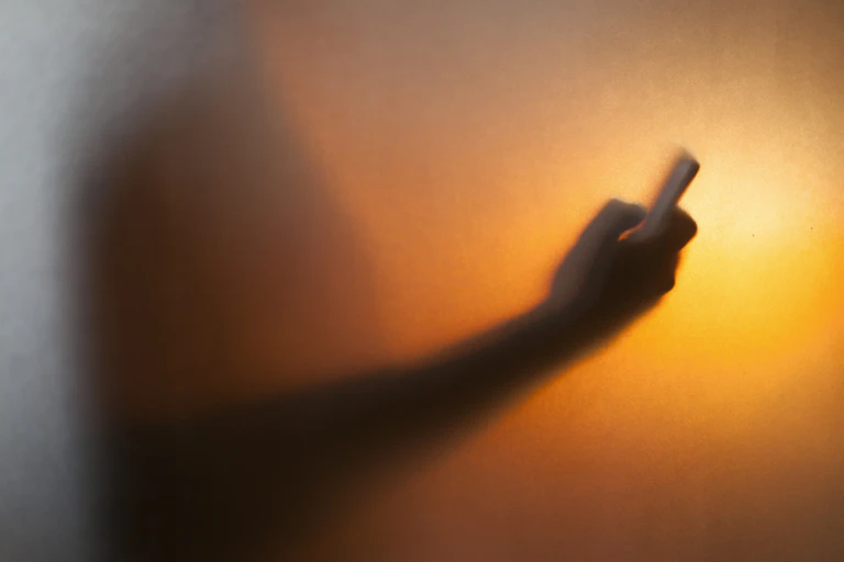 Black, orange and yellow illustration of silhouetted arm holding a smartphone.