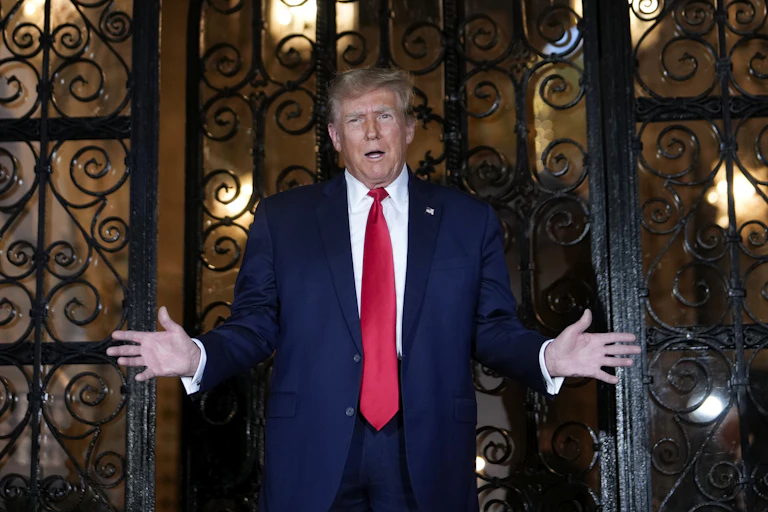 Man in red tie and dark suits stands with hands wide