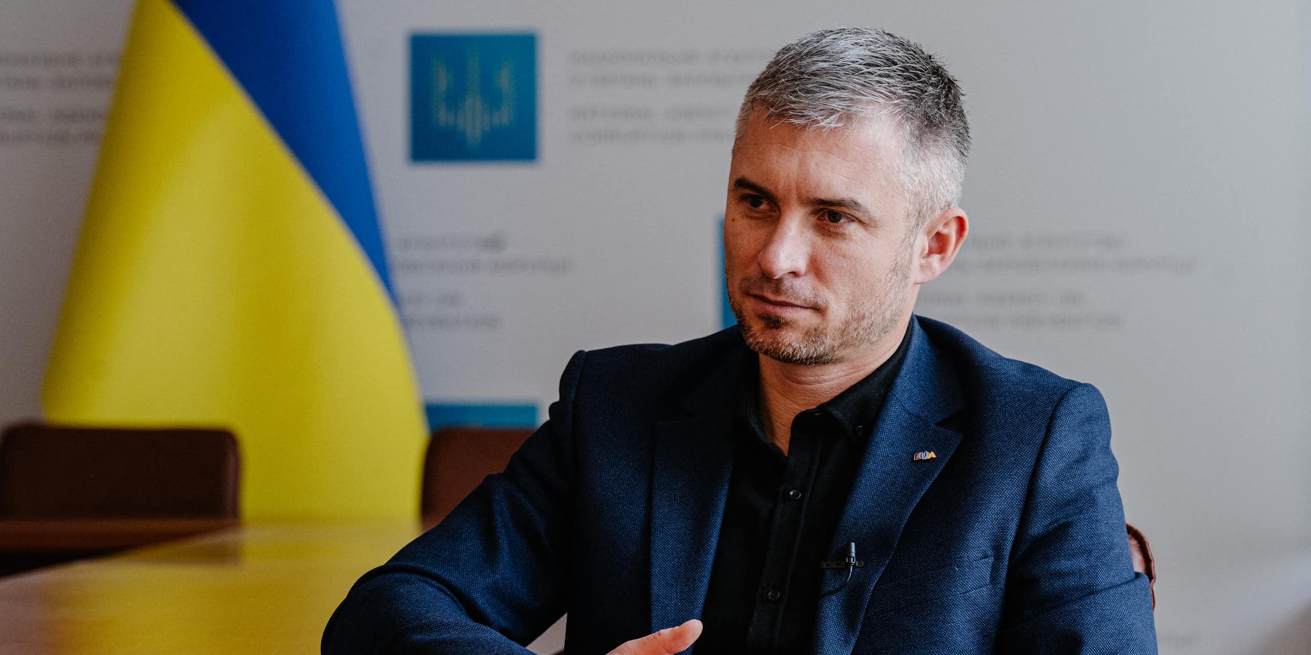 Un homme assis à un bureau, avec le drapeau ukrainien en arrière-fond