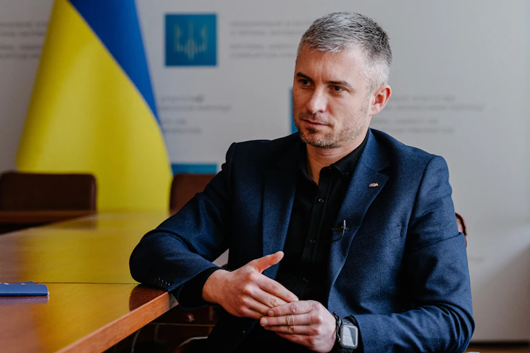 Un homme assis à un bureau, avec le drapeau ukrainien en arrière-fond